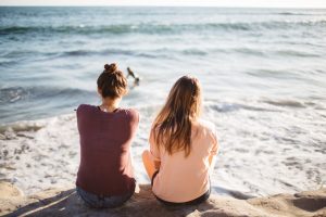 Two young women sitting on a rock looking at the ocean | Friends Blog Post by Heidi McBain, Women's Counselor in Flower Mound, Texas